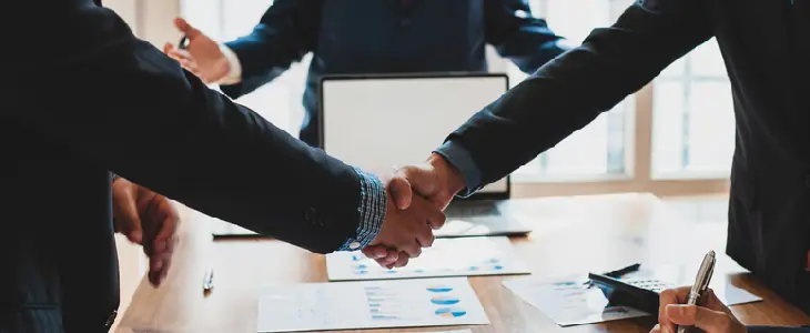 Lawyer and two clients shaking hands at a table after a successful arbitration