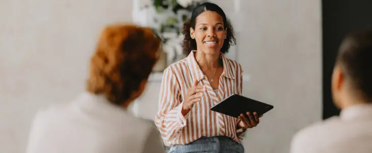 Confident businesswoman leading a group business meeting at a bright beige office. Professional interaction and teamwork concept.